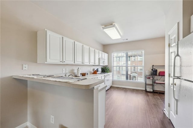 kitchen with white cabinets, light countertops, a peninsula, white appliances, and dark wood-style floors