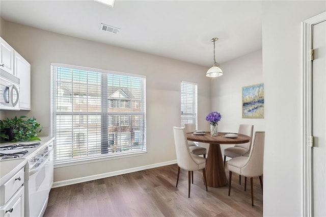 dining room featuring baseboards, visible vents, wood finished floors, and a healthy amount of sunlight