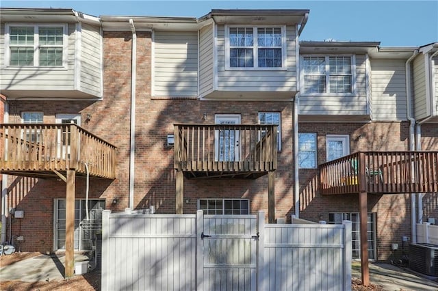 back of property featuring brick siding, fence, cooling unit, and a gate