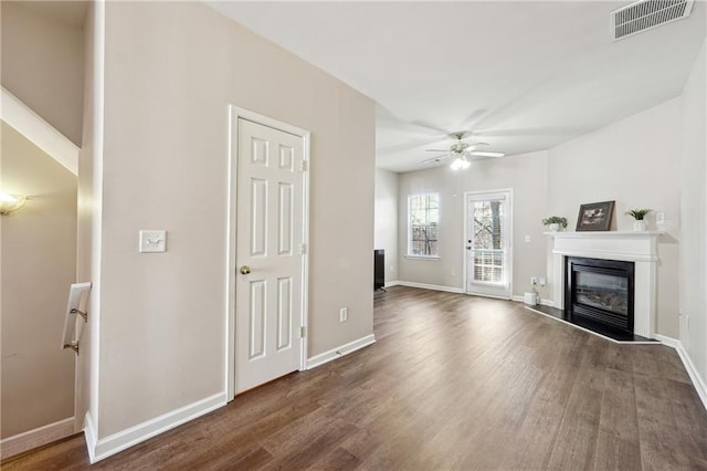 unfurnished living room with a ceiling fan, wood finished floors, a glass covered fireplace, and visible vents