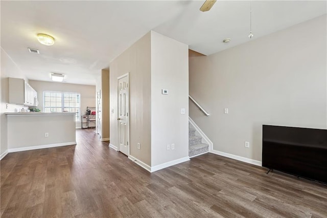 unfurnished living room with stairway, baseboards, dark wood finished floors, visible vents, and a ceiling fan