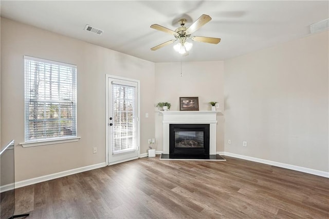 unfurnished living room with visible vents, a healthy amount of sunlight, a glass covered fireplace, and wood finished floors