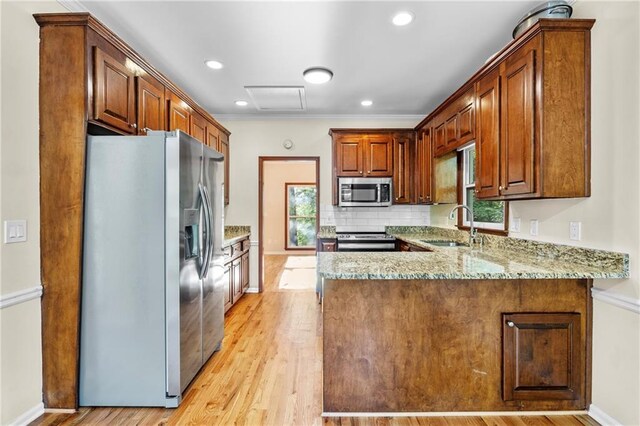kitchen with a sink, light stone counters, stainless steel appliances, and a peninsula