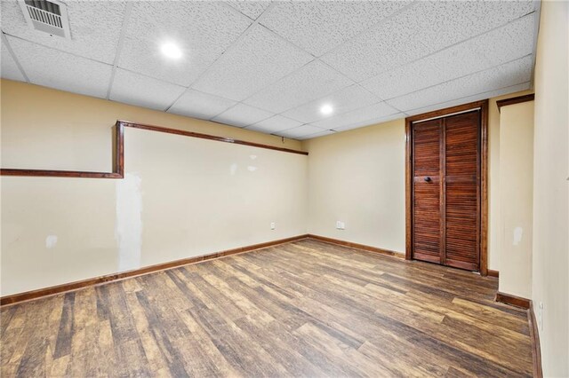 finished below grade area featuring baseboards, visible vents, a drop ceiling, and wood finished floors