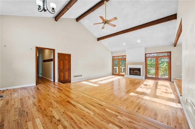 unfurnished living room featuring beam ceiling, ceiling fan with notable chandelier, baseboards, wood finished floors, and visible vents