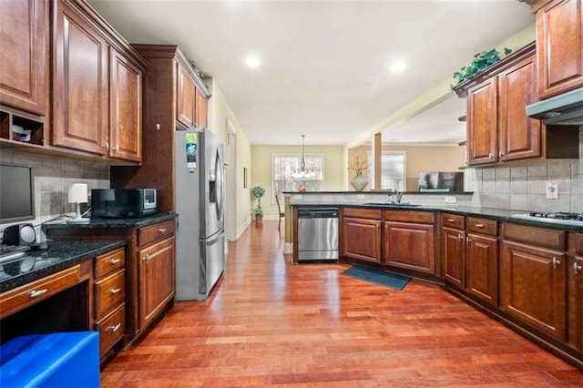 kitchen with a sink, light wood finished floors, appliances with stainless steel finishes, a peninsula, and decorative backsplash