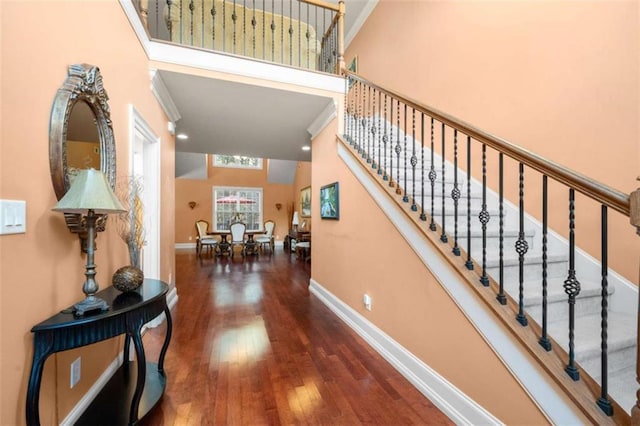 stairway featuring baseboards, a high ceiling, and hardwood / wood-style flooring