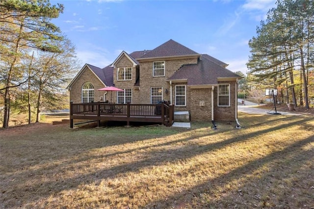 rear view of property featuring a wooden deck, brick siding, and a lawn