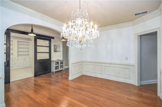 unfurnished dining area featuring crown molding, hardwood / wood-style floors, and a notable chandelier