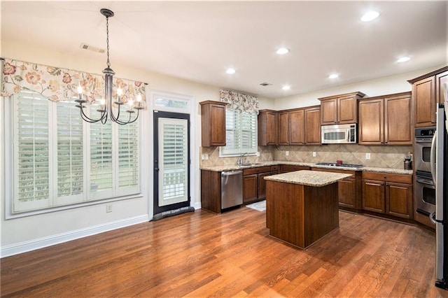 kitchen featuring light stone countertops, appliances with stainless steel finishes, a kitchen island, dark hardwood / wood-style flooring, and pendant lighting