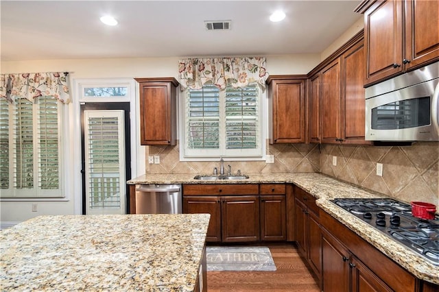 kitchen featuring backsplash, appliances with stainless steel finishes, dark hardwood / wood-style flooring, light stone countertops, and sink