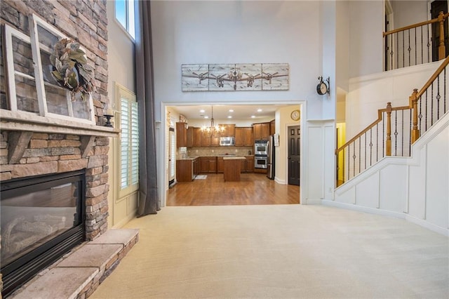 living room featuring a notable chandelier, a towering ceiling, light wood-type flooring, and a fireplace