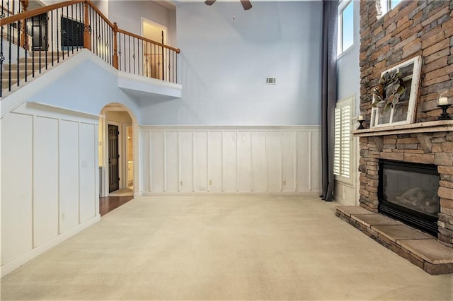 unfurnished living room featuring light carpet, a towering ceiling, a fireplace, and ceiling fan