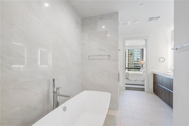 ensuite bathroom featuring a freestanding tub, visible vents, connected bathroom, tile walls, and vanity