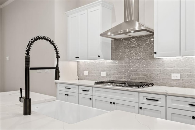 kitchen with white cabinetry, backsplash, light stone counters, stainless steel gas cooktop, and wall chimney exhaust hood