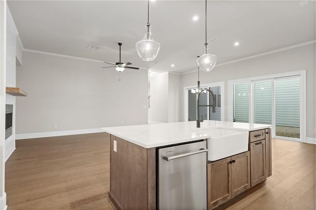 kitchen with sink, crown molding, hanging light fixtures, stainless steel dishwasher, and an island with sink