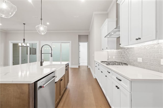 kitchen featuring pendant lighting, white cabinets, a kitchen island with sink, stainless steel appliances, and wall chimney range hood