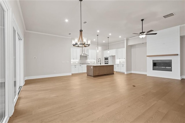 unfurnished living room with crown molding, light hardwood / wood-style flooring, a large fireplace, and ceiling fan