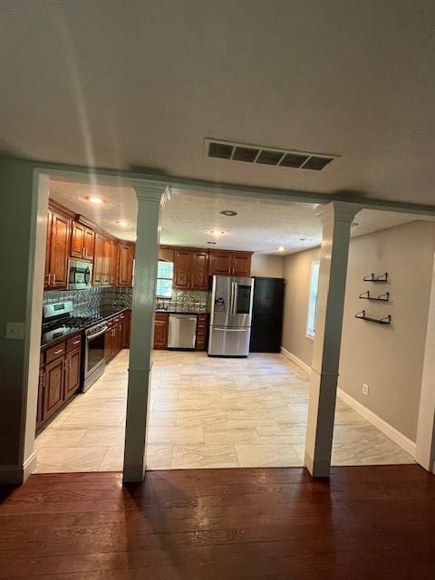 kitchen featuring tasteful backsplash, appliances with stainless steel finishes, light wood-type flooring, and ornate columns