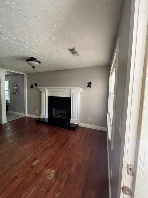 unfurnished living room with plenty of natural light, a textured ceiling, and dark hardwood / wood-style flooring