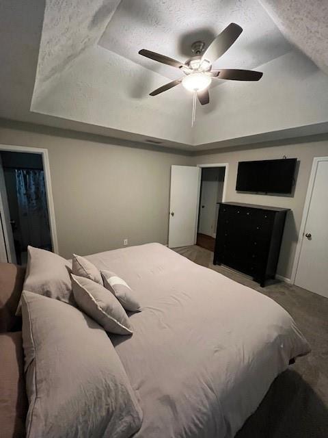 carpeted bedroom featuring ceiling fan, a raised ceiling, and a textured ceiling