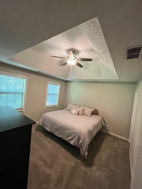 carpeted bedroom with a raised ceiling, a textured ceiling, and ceiling fan