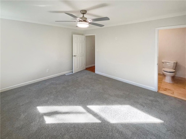 unfurnished bedroom with ensuite bath, ceiling fan, and dark colored carpet