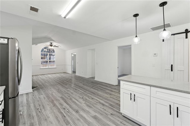 kitchen featuring decorative light fixtures, stainless steel refrigerator, ceiling fan, a barn door, and white cabinets