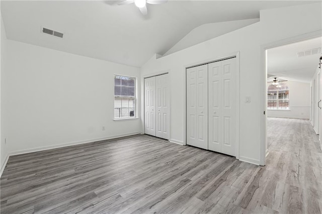 unfurnished bedroom featuring lofted ceiling, two closets, ceiling fan, and light hardwood / wood-style flooring