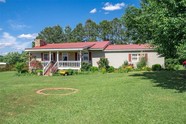 ranch-style home featuring metal roof, a porch, a front lawn, and a chimney