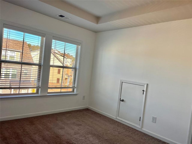 empty room featuring a healthy amount of sunlight, a tray ceiling, and dark colored carpet