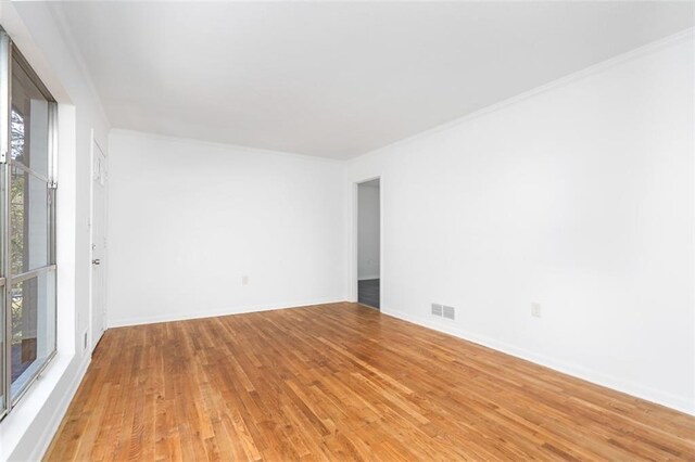 empty room featuring ornamental molding, light wood-type flooring, visible vents, and baseboards