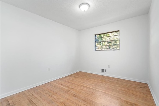 unfurnished room featuring light wood-style floors, baseboards, visible vents, and a textured ceiling