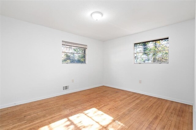 empty room with baseboards, visible vents, and light wood finished floors