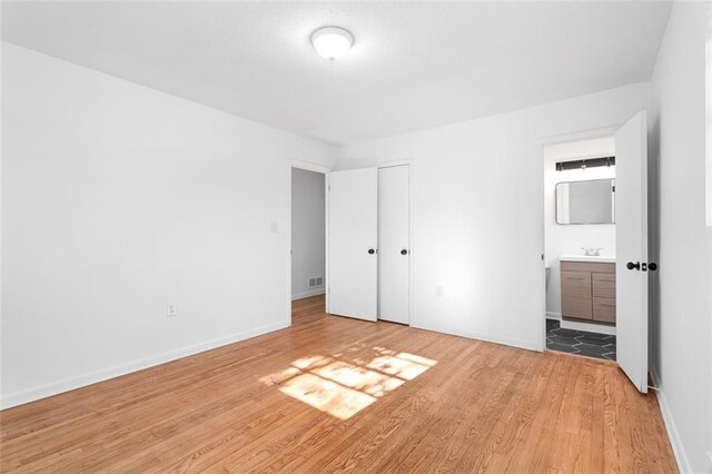 unfurnished bedroom with a closet, baseboards, ensuite bath, light wood-type flooring, and a sink