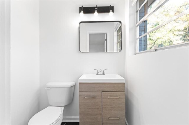 half bath featuring baseboards, vanity, and toilet