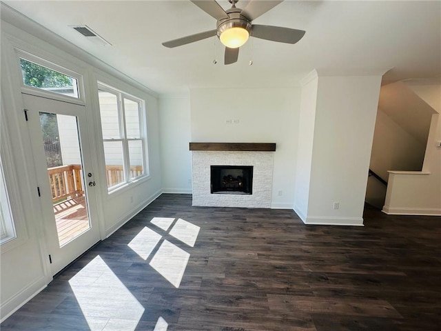 unfurnished living room with ceiling fan, a stone fireplace, and dark wood-type flooring