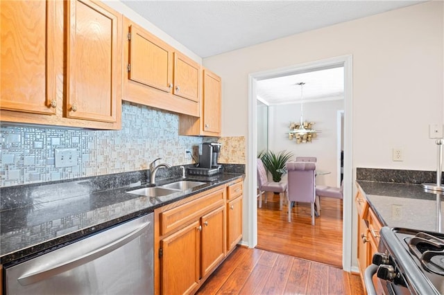 kitchen with a sink, tasteful backsplash, wood-type flooring, appliances with stainless steel finishes, and an inviting chandelier