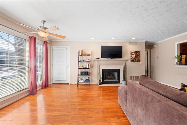 living room featuring visible vents, a high end fireplace, ornamental molding, a textured ceiling, and light wood-type flooring