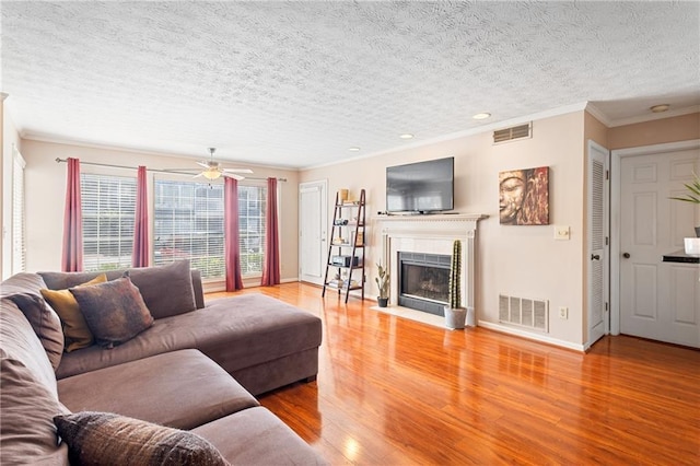 living area featuring visible vents, ornamental molding, a fireplace with flush hearth, and wood finished floors