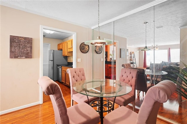 dining room featuring baseboards, a textured ceiling, and light wood finished floors