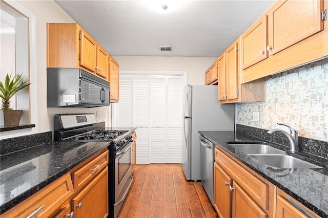 kitchen featuring visible vents, a sink, decorative backsplash, stainless steel appliances, and dark wood-style flooring