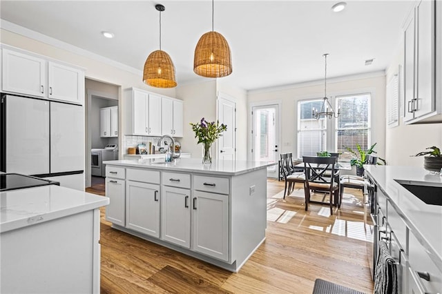 kitchen with independent washer and dryer, white cabinets, a kitchen island with sink, and built in fridge