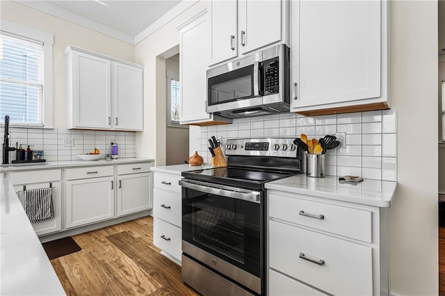 kitchen with white cabinets, stainless steel appliances, sink, light wood-type flooring, and crown molding