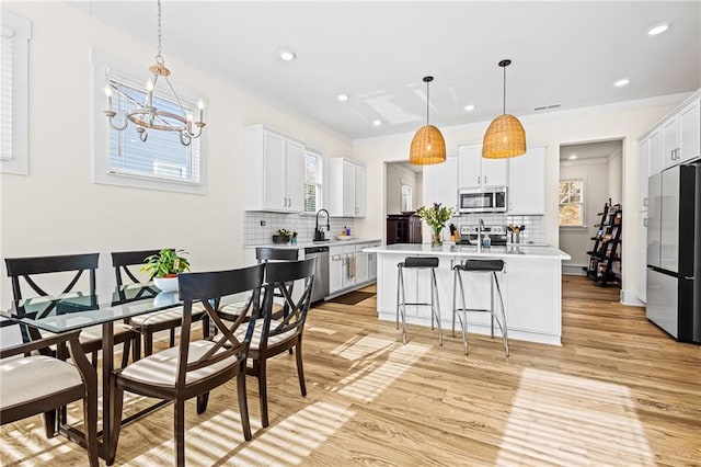 kitchen with white cabinets, stainless steel appliances, hanging light fixtures, and a center island with sink