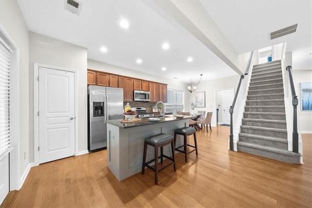 3607 Archgate Ct, Alpharetta, GA 30004 - kitchen with stainless steel appliances, an island with sink, light wood-type flooring, brown cabinetry, and a kitchen bar