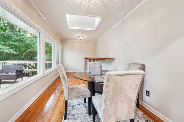 dining area with wood-type flooring, ornamental molding, and a skylight