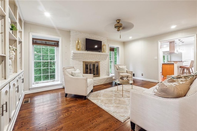 living room featuring dark hardwood / wood-style flooring, a brick fireplace, and ceiling fan