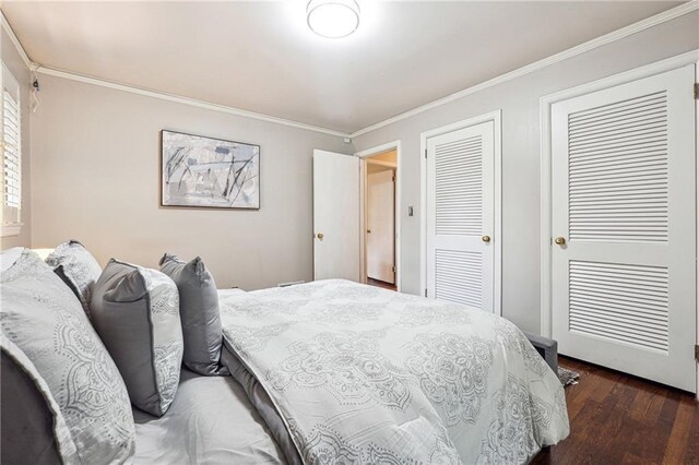 bedroom with ornamental molding, dark wood-type flooring, and two closets