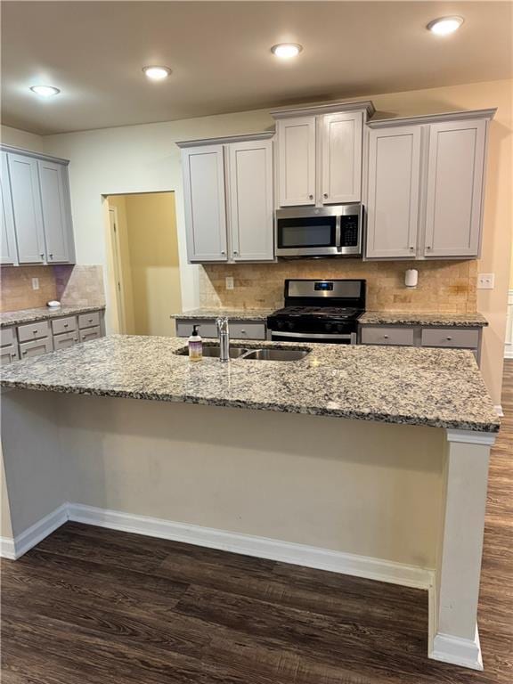 7703 Hansel Ln, Lithonia, GA 30058 - kitchen with stainless steel appliances, dark wood-type flooring, light stone countertops, an island with sink, and decorative backsplash